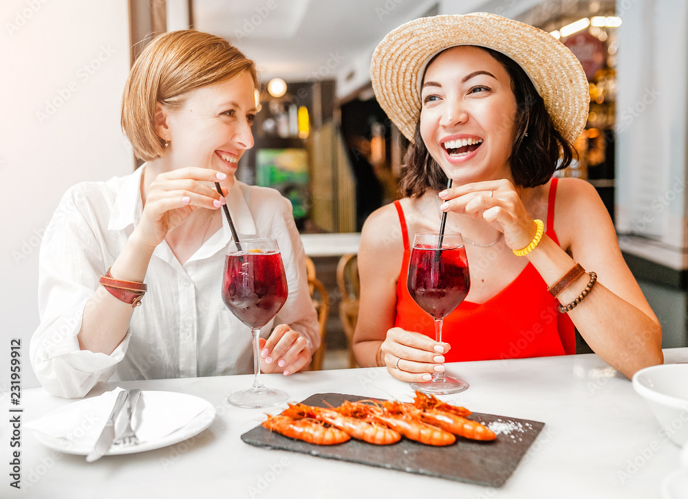 Two happy cheerful girl friends drinking wine and having lunch at seafood restaurant Two happy cheerful girl friends drinking wine and having lunch at seafood restaurant