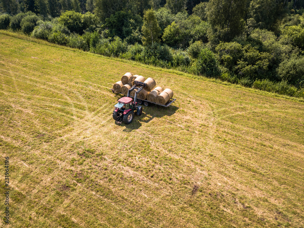 Obraz premium Aerial Drone Photo of Farmer Harvesting Hay Rolls in the Wheat Field with a Red Tractor