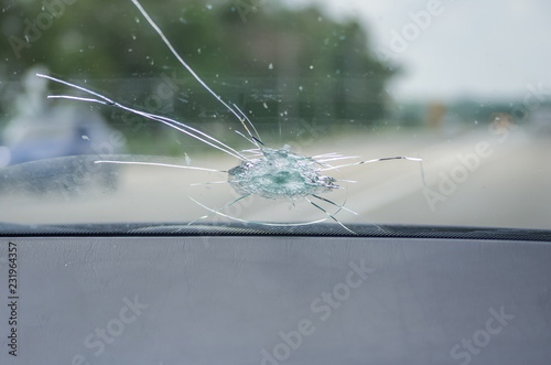 The broken windshield of the car from flying stone. The hole in the glass, chips and debris, cracks in strips. The glass reflects the sky with clouds. photo