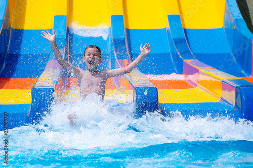 Cheerful boy splashing water on water slide at aqua park