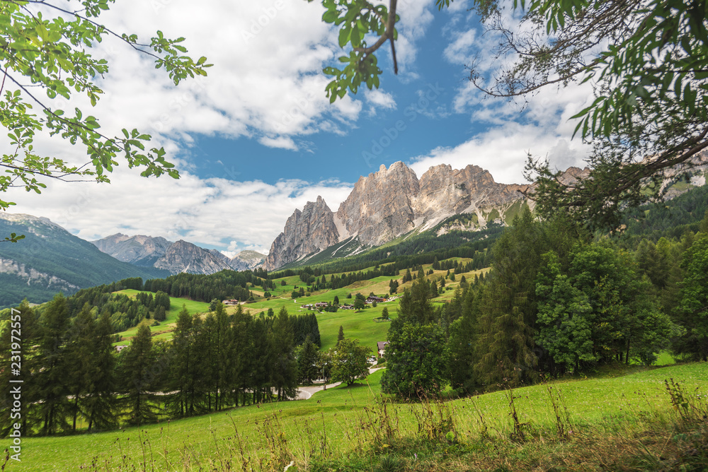 Green grass and blue sky with clouds around high mountains, Dolomites in Italy.