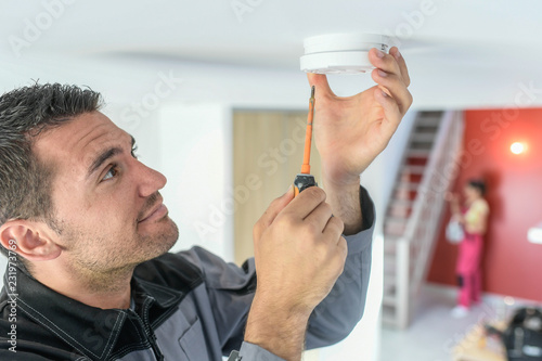 Male technician is fitting a fire alarm in the ceiling