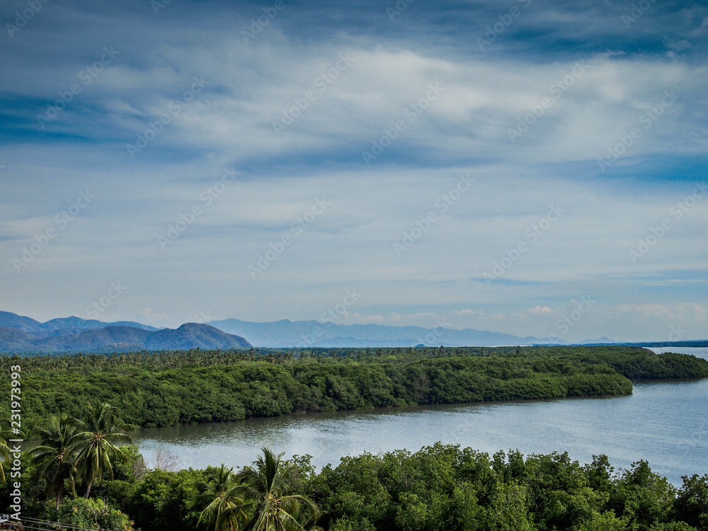 Cuyutlan Lagoon surrounded by tropical vegetation, calm waters, mountains and a cloudy sky with abundant clouds in the background, spring in Manzanillo, Colima Mexico Cuyutlan Lagoon surrounded by tropical vegetation, calm waters, mountains and a cloudy sky with abundant clouds in the background, spring in Manzanillo, Colima Mexico