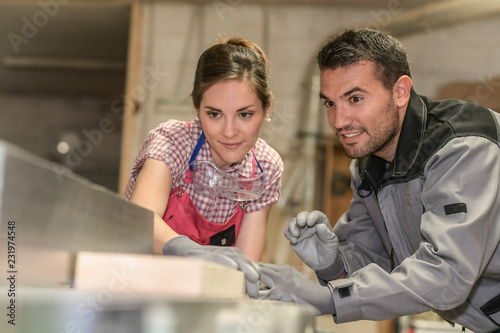 Female trainee and male mentor cutting a piece of wood in workshop