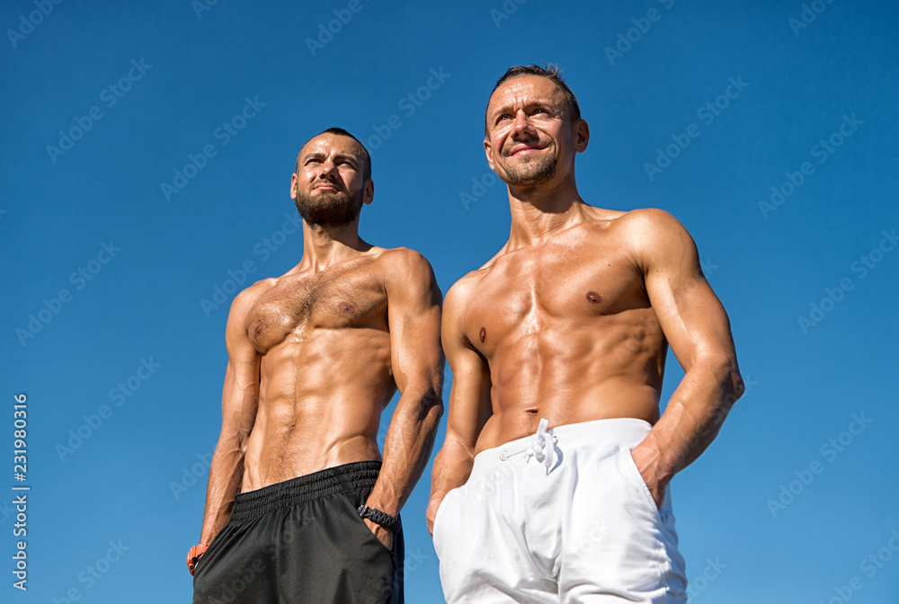 Fototapeta premium Men sexy muscular bare torso stand outdoor. Men muscular body posing confidently with hands in pockets. Sportsmen muscular belly posing. Sport and bodycare. Muscular masculine guys look confident