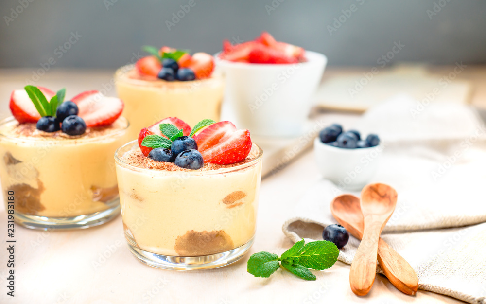 homemade, exquisite dessert tiramisu in glasses decorated with strawberry, blueberry, mint on white wooden table homemade, exquisite dessert tiramisu in glasses decorated with strawberry, blueberry, mint on white wooden table