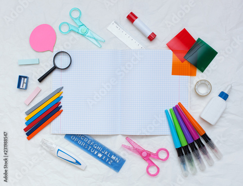 top view of a clean notebook and school supplies: rulers, scissors, pencils, felt-tip pens, stickers, glue, sharpener, eraser on a white paper background with space for text. back to school, flat lay