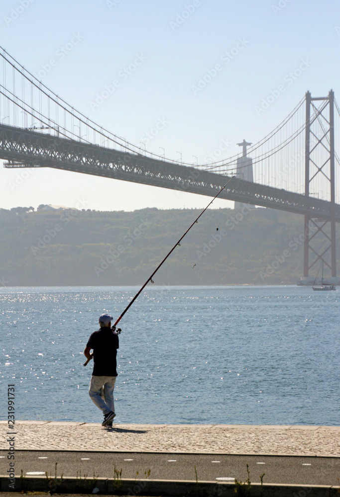 A man prepares to throw out his fishing rod near Ponte 25 de Abril in Lisbon, Portugal, on a sunny day