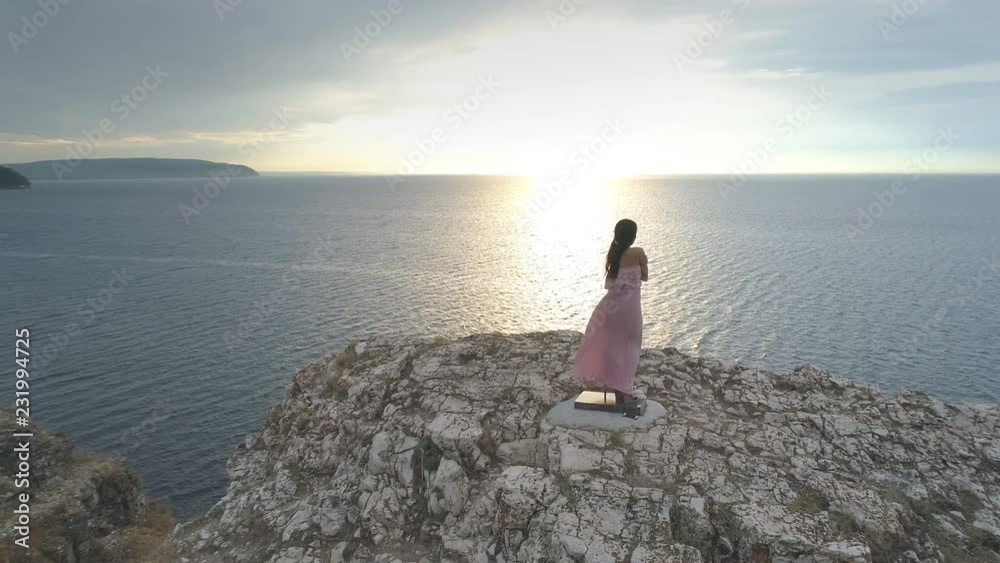 Aerial view on a young woman in a dress stands on the edge of a cliff Aerial view on a young woman in a dress stands on the edge of a cliff