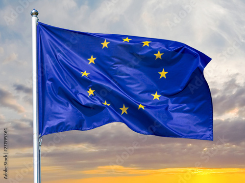 Flag of the European Union waving in the wind on flagpole against background of the sunrise, close-up