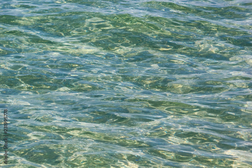 Transparent sea water surface in the rays of the summer sun, background, texture
