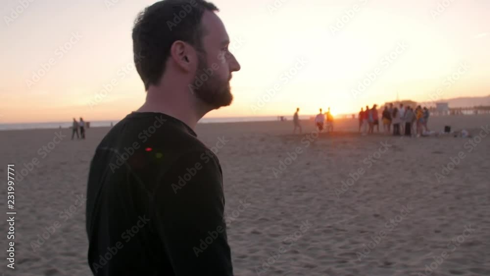 Man walking toward group of friends on beach at sunset Man walking toward group of friends on beach at sunset