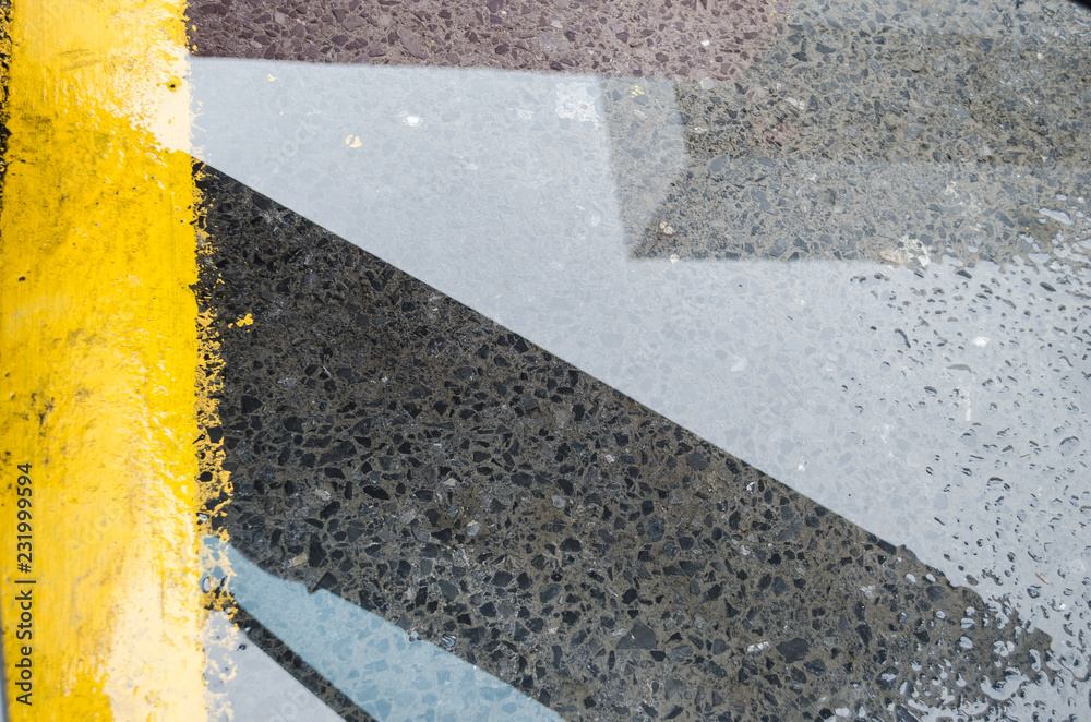 Fototapeta premium Reflection of an urban building on a puddle of water on the street, yellow line parking place