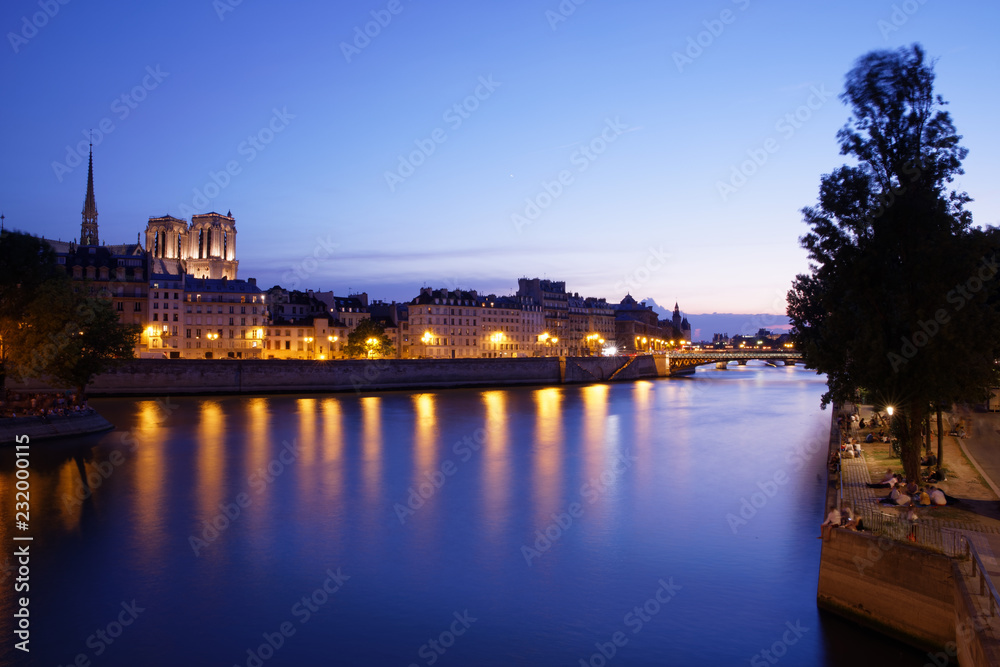 Fototapeta premium Paris, France - July 5, 2018: Notre Dame Cathedral with Paris cityscape and River Seine at dusk, France