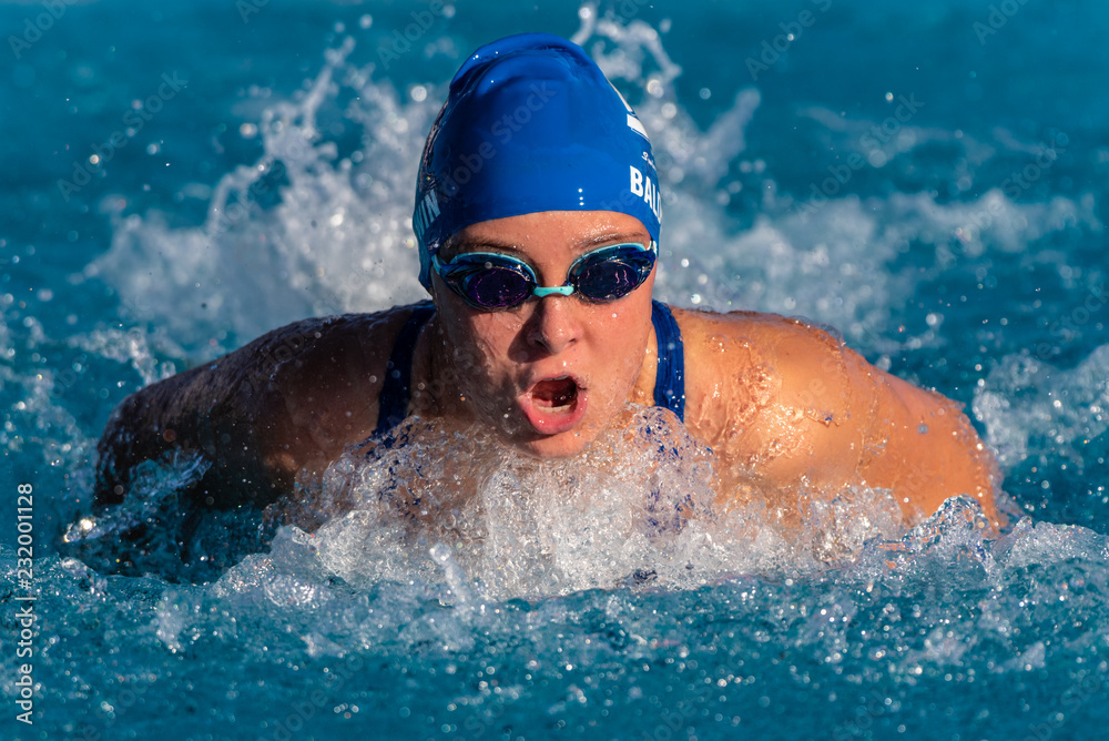 Competitive female swimmer coming up to breathe during powerful butterfly stroke during race.