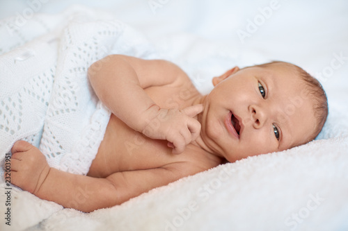 Little newborn baby boy sleeping in white blanket, lying on bed.