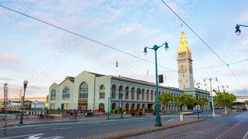 Day to night time-lapse of moving clouds, fast traffic on Embarcadero in front of iconic Ferry Building with Bay Bridge background in downtown San Francisco, California. 4k 30fps zoom out