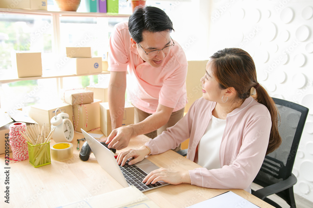 Fototapeta premium Couples asians business owner using laptop at home. Pointing at screen with happily.SME,check product order,Online selling, e-commerce, shipping concept.Midle-aged couple owner online business.