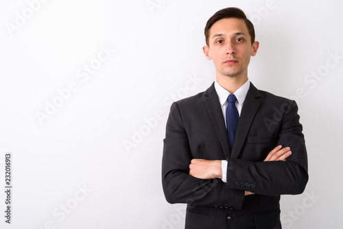 Studio shot of young handsome businessman with arms crossed agai