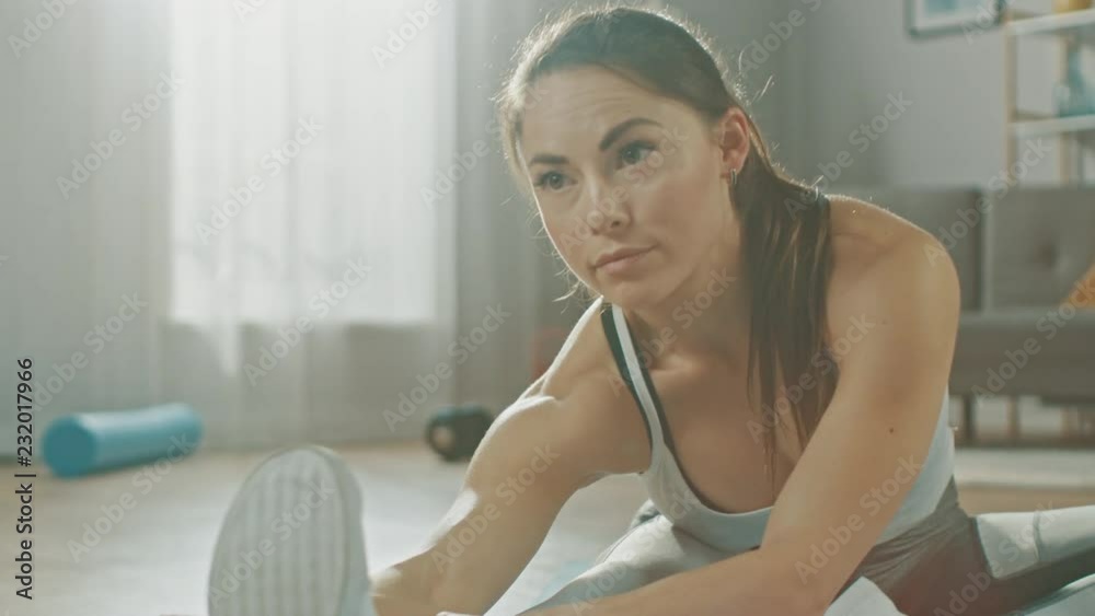 Close Up of a Beautiful Confident Fitness Girl in an Athletic Workout Clothes Doing Stretching Yoga Exercises in Her Bright and Spacious Living Room with Cozy Minimalistic Interior. Close Up of a Beautiful Confident Fitness Girl in an Athletic Workout Clothes Doing Stretching Yoga Exercises in Her Bright and Spacious Living Room with Cozy Minimalistic Interior.