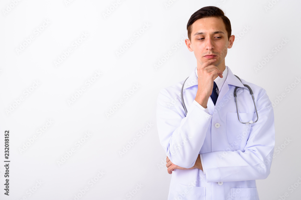 Studio shot of young handsome man doctor thinking while looking Studio shot of young handsome man doctor thinking while looking