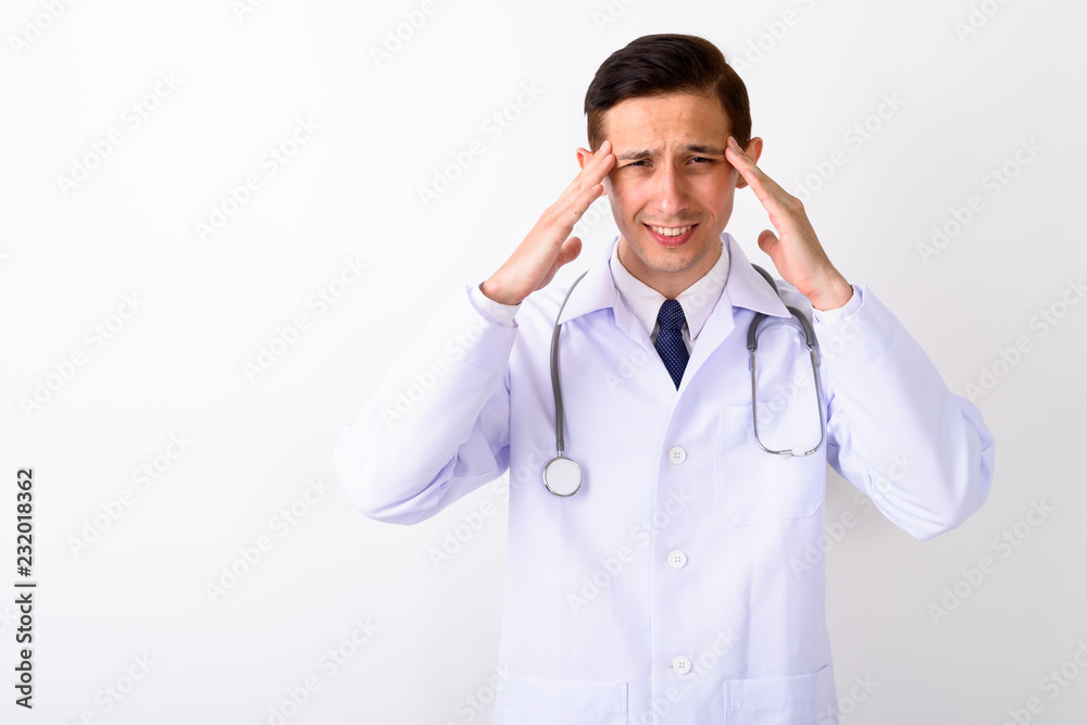 Studio shot of young stressed man doctor having headache against Studio shot of young stressed man doctor having headache against