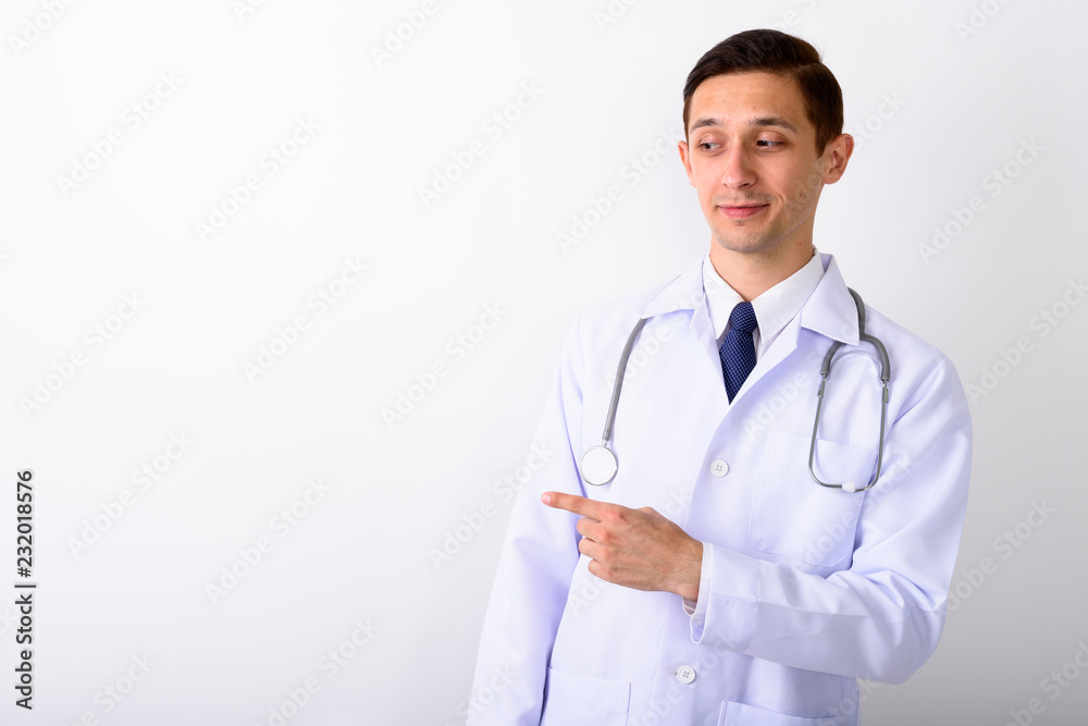 Studio shot of young handsome man doctor pointing to the side ag Studio shot of young handsome man doctor pointing to the side ag