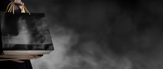 Black friday sale concept of young woman holding shopping bag on dark background with copy space fashion style