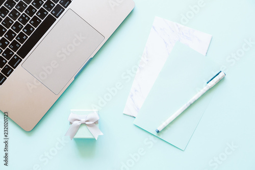 Flatlay of laptop, paper, pen and little gift box on a blue background
