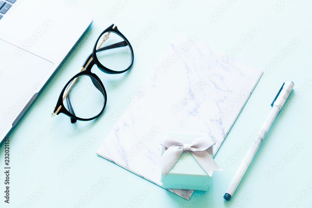 Flatlay of laptop, paper, pen, reading glasses and little gift box on a blue background Flatlay of laptop, paper, pen, reading glasses and little gift box on a blue background
