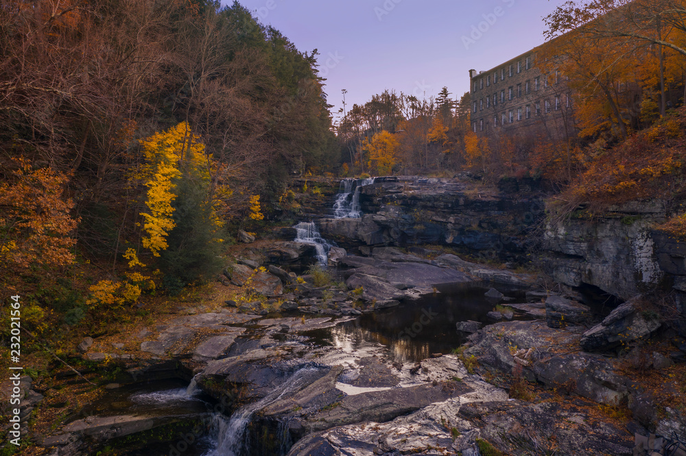 autumn waterfall scene with trees and old building in background
