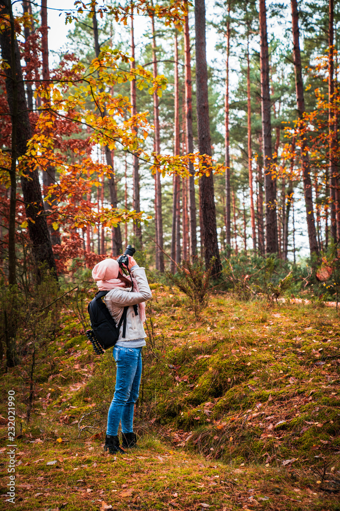 Young white girl taking photos of trees. Alone in the forest. Warm clothes. Autumn season Young white girl taking photos of trees. Alone in the forest. Warm clothes. Autumn season