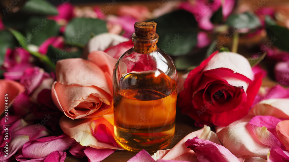 Φωτογραφία Aroma oil glass bottle among roses and petals on the table, natural raw material