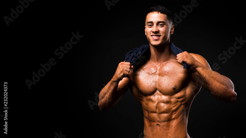 Portrait of handsome muscular guy with towel in the neck posing over a dark background. © Stavros