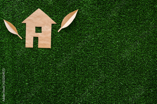 Green energy for home concept. Care for environment. House cutout made of craft paper on green grass background top view copy space