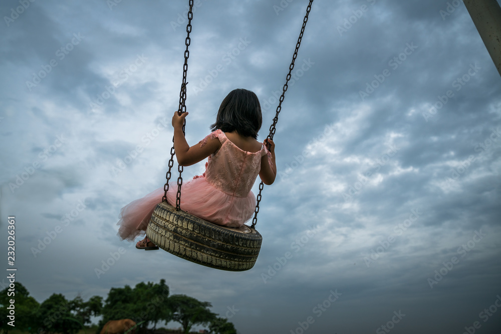Little girl with skirt play swing at outdoor park. Dramatic sky