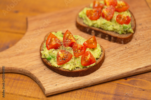 Avocado toast with cherry tomatoes on wooden background. Breakfast with avocado toast, vegetarian food.