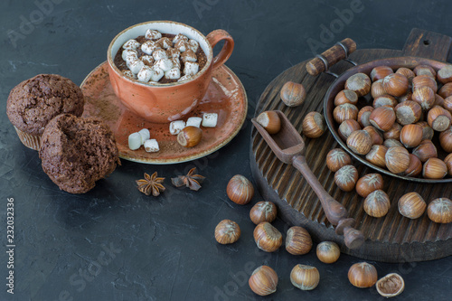 Hazelnuts, muffins and a cup of hot chocolate with marshmallow , on a table on a wooden stand