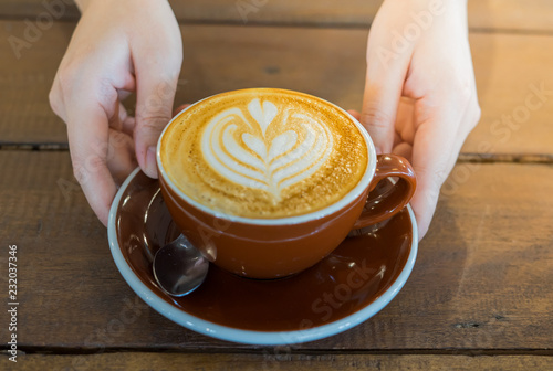 Close up of female hand serving coffee with latte art in the morning. Focus on female hands placing a cup of coffee.