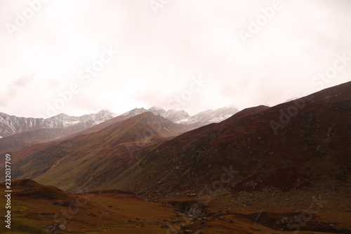 Mountains in autumn with brown and reddish grass under cloudy sky