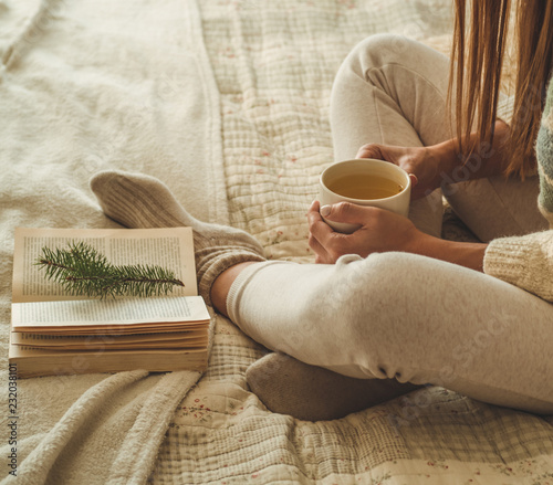 Cozy home. Beautiful girl is reading a book on the bed. Good morning with tea. Pretty young girl relaxing. The concept of reading