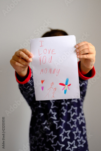 The boy is holding a hand-made postcard for Mother's Day "I love you mommy"