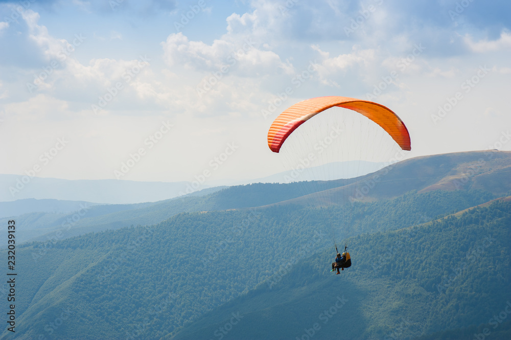 Paraglider fly over a mountain valley on a sunny summer day. Paragliding in the Carpathians in the summer. Paraglider fly over a mountain valley on a sunny summer day. Paragliding in the Carpathians in the summer.