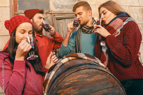 Smiling european men and women during party photoshoot. The guys posing as friends at studio fest with wineglasses with hot mulled wine on foreground.