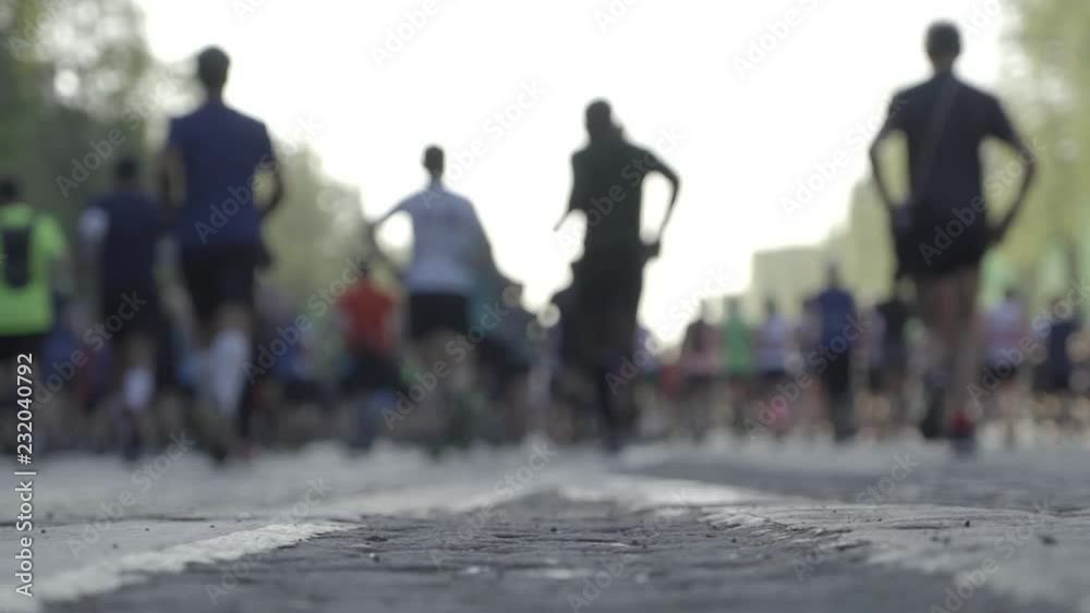 Low angle slow motion shot of marathon runners viewed from behind, right after the start