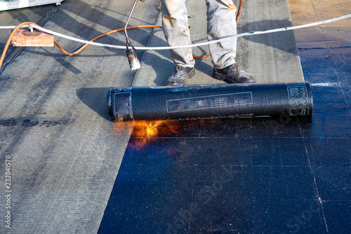 Worker preparing part of bitumen roofing felt roll for melting by gas heater torch flame photo