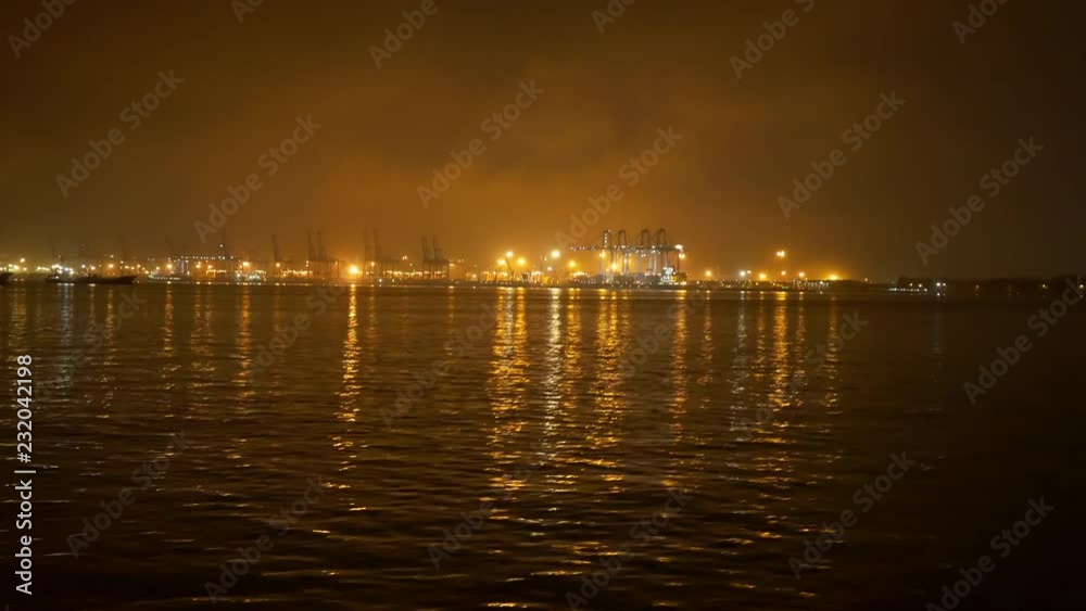 A boat ride at night passing a buoy overlooking a brightly lit industrial port at night A boat ride at night passing a buoy overlooking a brightly lit industrial port at night