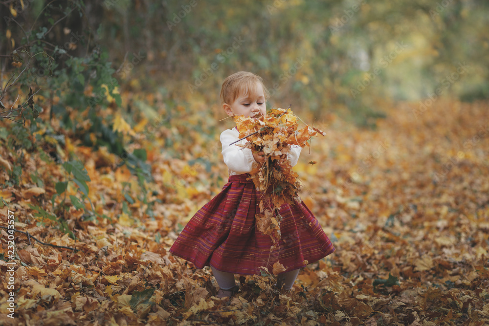 Cute little girl playing with leaves in outdoors in the park during an autumn day Cute little girl playing with leaves in outdoors in the park during an autumn day