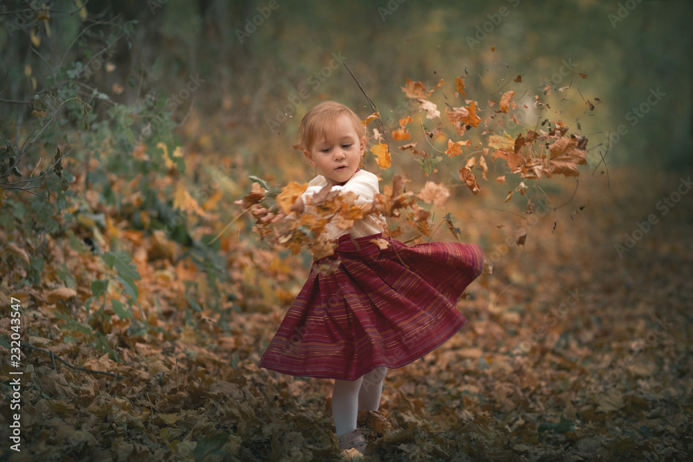 Cute little girl playing with leaves in outdoors in the park during an autumn day Cute little girl playing with leaves in outdoors in the park during an autumn day