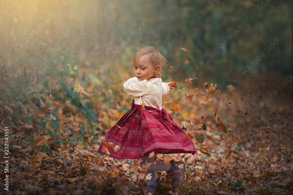 Cute little girl playing with leaves in outdoors in the park during an autumn day Cute little girl playing with leaves in outdoors in the park during an autumn day